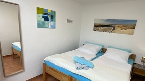 Un dormitorio con cama, espejo, una obra de arte en la pared y una mesita de noche con lámpara.