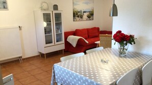 Un área de comedor con una mesa cubierta con un mantel de lunares, un jarrón con flores rojas y un sofá rojo.