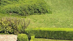 Un jardin aménagé avec un sentier en pierre, des haies soigneusement taillées et une vue sur la mer où l’on peut apercevoir des voiliers.