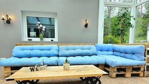 Een blauwe hoekbank met een houten salontafel ervoor, een raam met uitzicht op groen, en wandlampen.