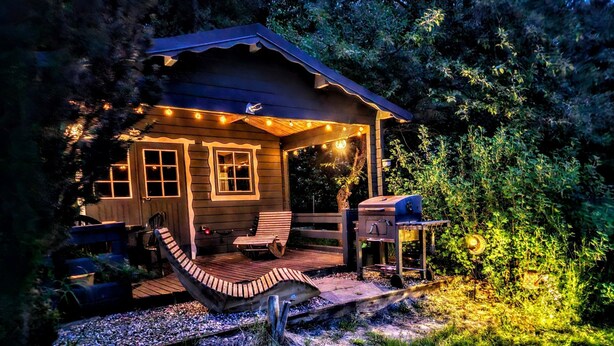Een houten chalet met een veranda, een barbecue en sfeerverlichting.