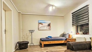 Ein Schlafzimmer mit Bett, Nachttisch, Lampe, einem Fenster mit Jalousien, einer Heizung und einem Bild an der Wand.