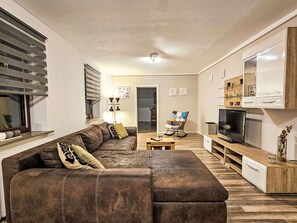 A living room with a brown sofa, a wooden coffee table, a television, and a bookshelf. - Apartment Naturpark by Interhome (Selk)