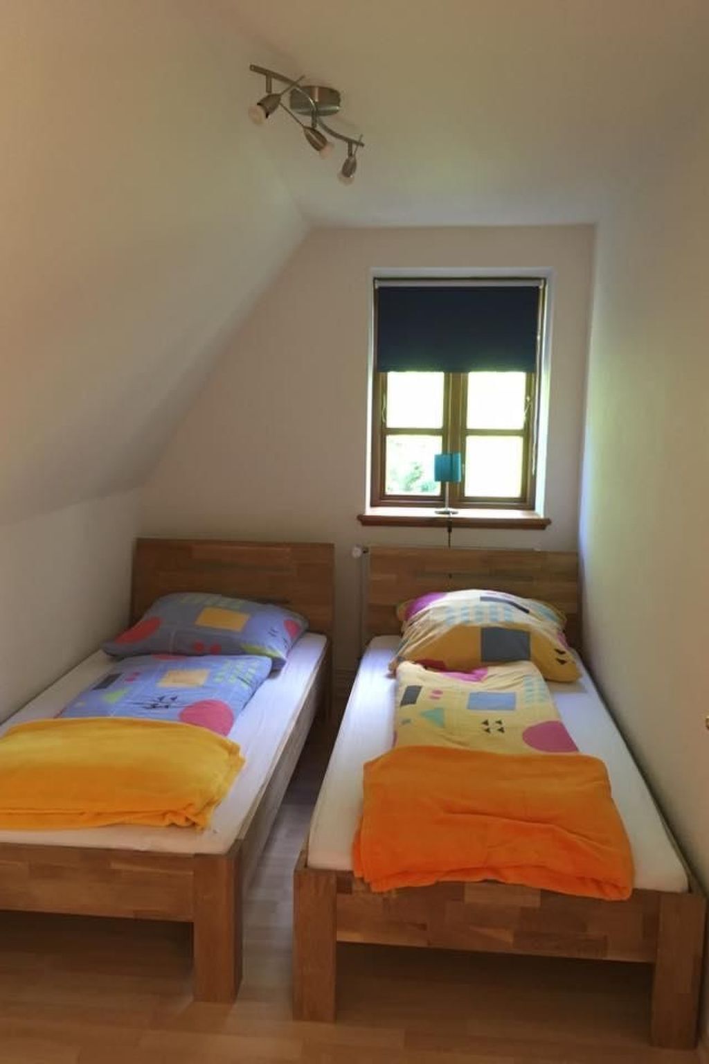 Ein kleines Schlafzimmer im Dachgeschoss mit zwei Holzbettklappen, einem Fenster mit Aussicht und einer Deckenleuchte.