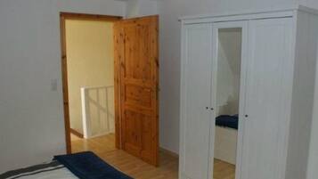 A room with a bed, a wardrobe, and a door leading to another room.