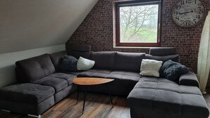 Un soggiorno in stile loft con parete in mattoni, un'ampia finestra, un divano componibile, un tavolino in legno e una sveglia a parete.