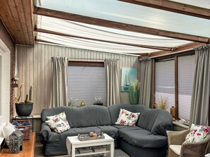 Een gezellige woonkamer met een grijze bank, een kleine witte tafel en een rieten stoel.