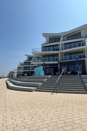A modern multi-story building with a curved facade, outdoor seating area, and a clear sky. - Achtern Diek by Interhome (Laboe)