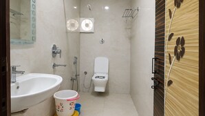 Une salle de bain équipée d’un lavabo, de toilettes, d’une douche et d’un petit tabouret muni d’un récipient.