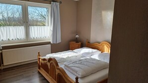 Une chambre à coucher avec un lit en bois, une table de chevet, une lampe, une fenêtre avec des rideaux et un radiateur.
