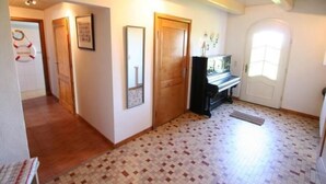 Ein Korridor mit Fliesenboden, Holztüren und einem Klavier.