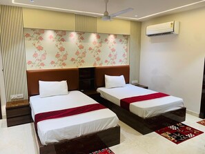 A hotel room with two beds, a ceiling fan, an air conditioning unit, and a floral wallpaper design. - Hotel Relax (Agra)