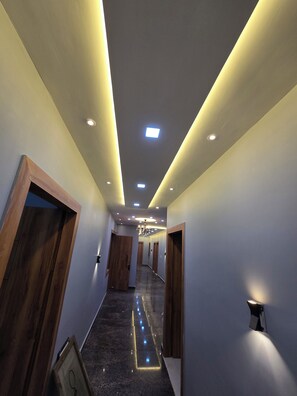A modern hallway with recessed lighting, wooden doors, and a marble floor. - Hotel Relax (Agra)