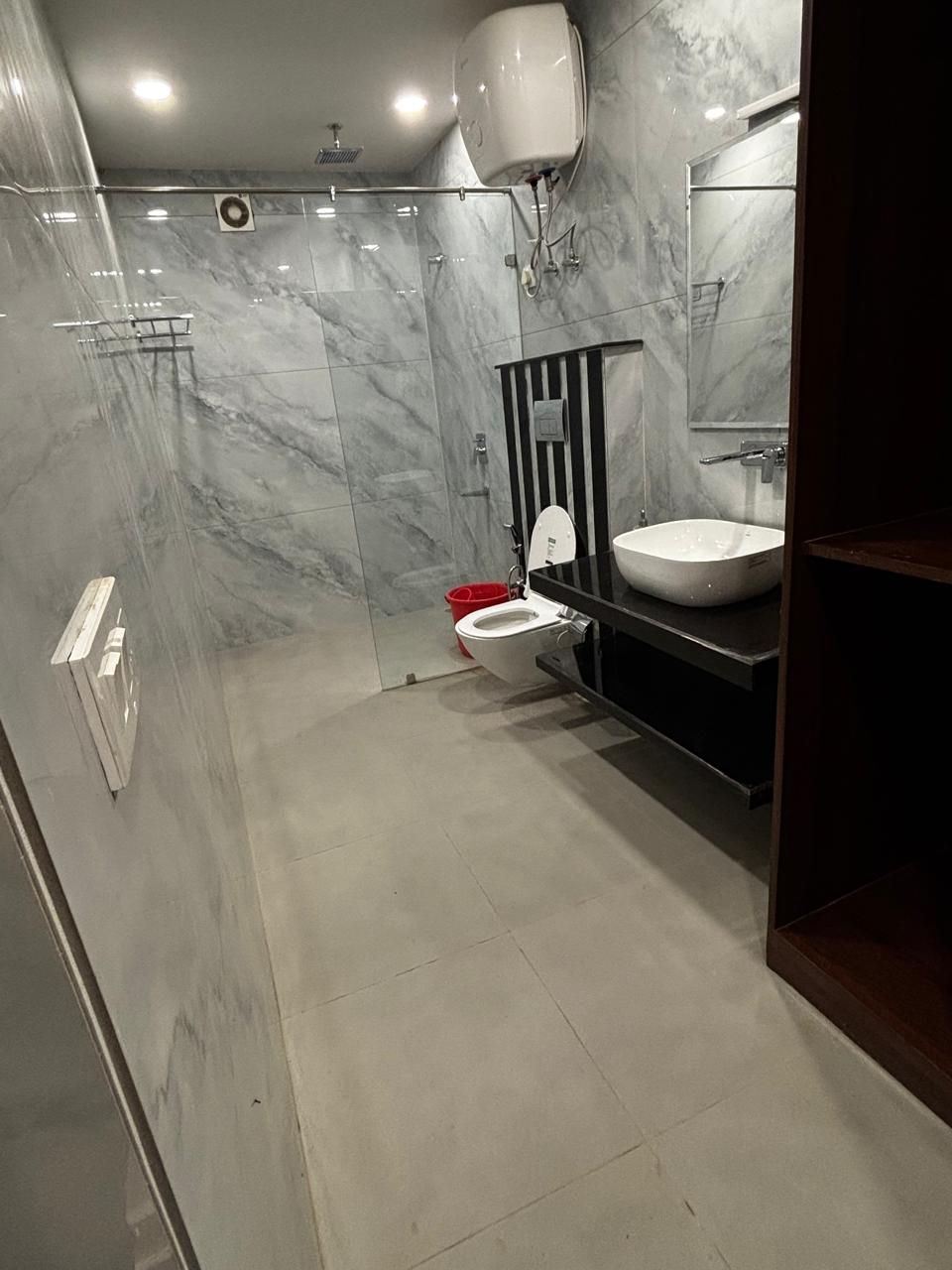 Un bagno moderno con un WC bianco, un lavandino nero e zona doccia con piastrelle in marmo.