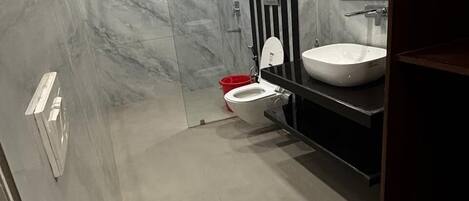 Un bagno moderno con un WC bianco, un lavandino nero e zona doccia con piastrelle in marmo.