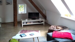 Ein Loft-Wohnzimmer mit freiliegenden Holzbalken, einer weißen Medienwand, einem Fernseher und einem Oberlicht.