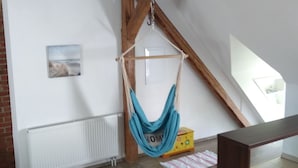Ein Zimmer mit freiliegenden Holzbalken, einer Hängematte, einem Heizkörper, einer Holzbank und einem kleinen Tisch.