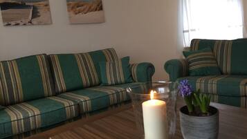Ein Wohnzimmer mit einem grünen Sofa, einem Glastisch mit einer Kerze und einer Zimmerpflanze.