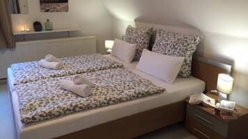 Ein Doppelbett mit gemusterten Betttextilien, zwei Kissen, ein Nachttisch mit Lampe und ein kleines Regal mit Dekoration.