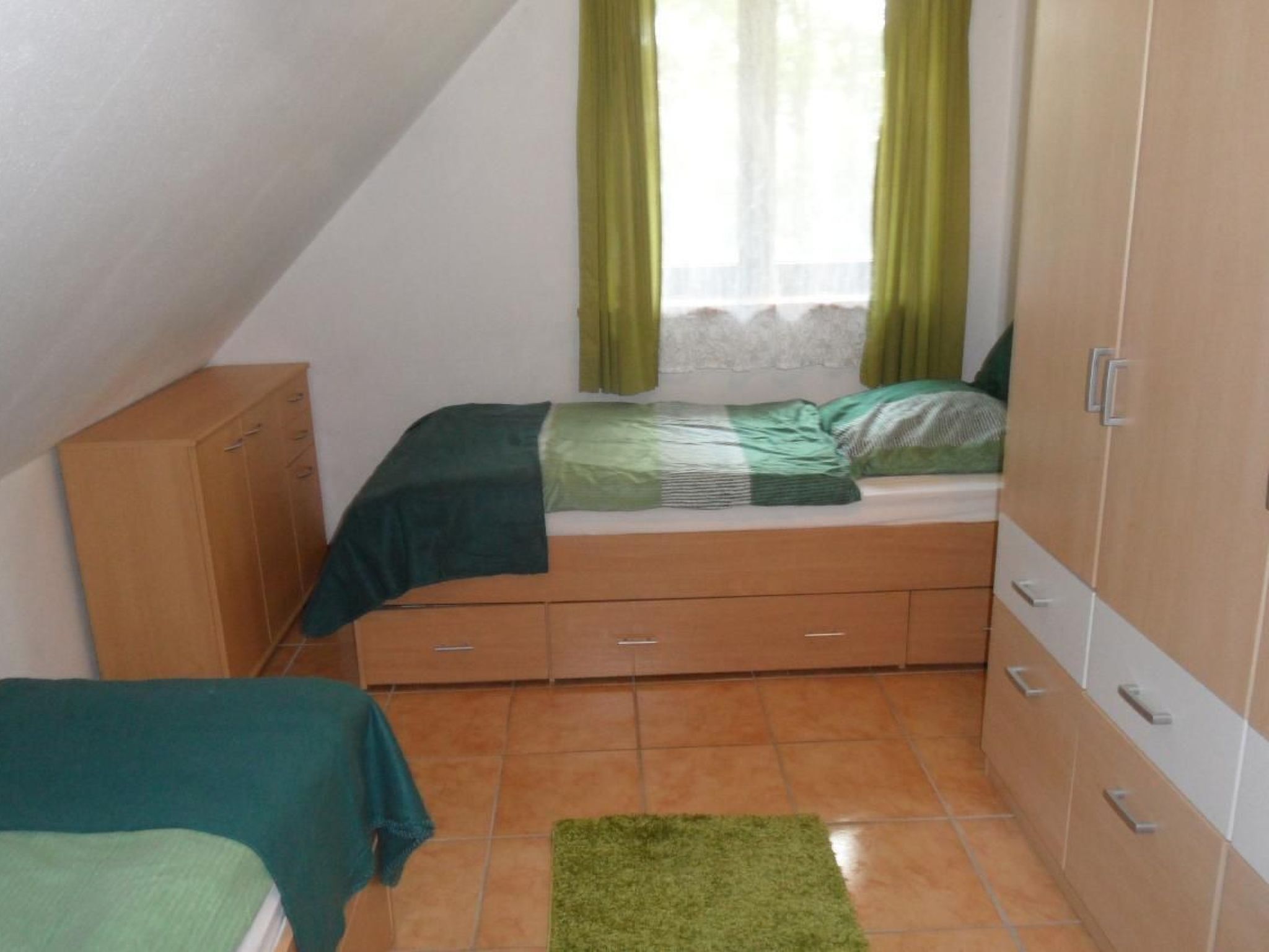 Une petite pièce, de taille modeste, comprenant un lit, une armoire et une fenêtre avec des rideaux.