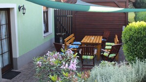 A patio with a wooden table and chairs, surrounded by plants and a green canopy. - Geräumige Ferienwohnung mit Terrasse, in günstiger zentraler Lage in der Oberla by Interhome (Elstra)