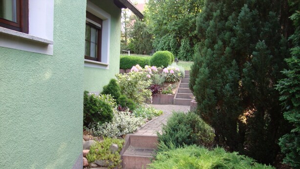 A green house with a stone pathway leading to a door. - Geräumige Ferienwohnung mit Terrasse, in günstiger zentraler Lage in der Oberla by Interhome (Elstra)