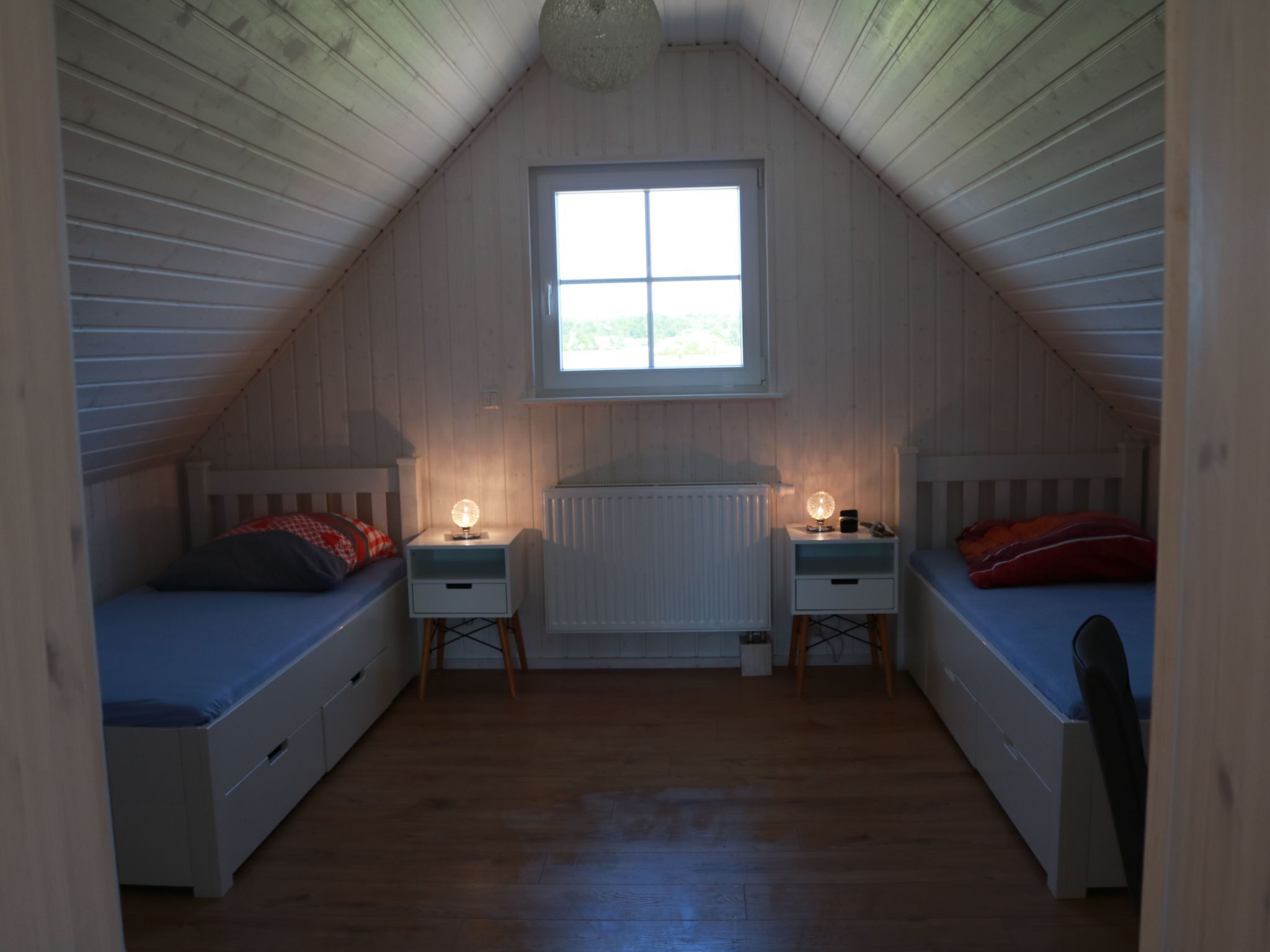 A small attic bedroom with two single beds, a window, and a radiator.