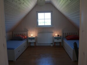 Ein kleines Schlafzimmer im Dachgeschoss mit zwei Einzelbetten, einem Fenster und einer Heizung.