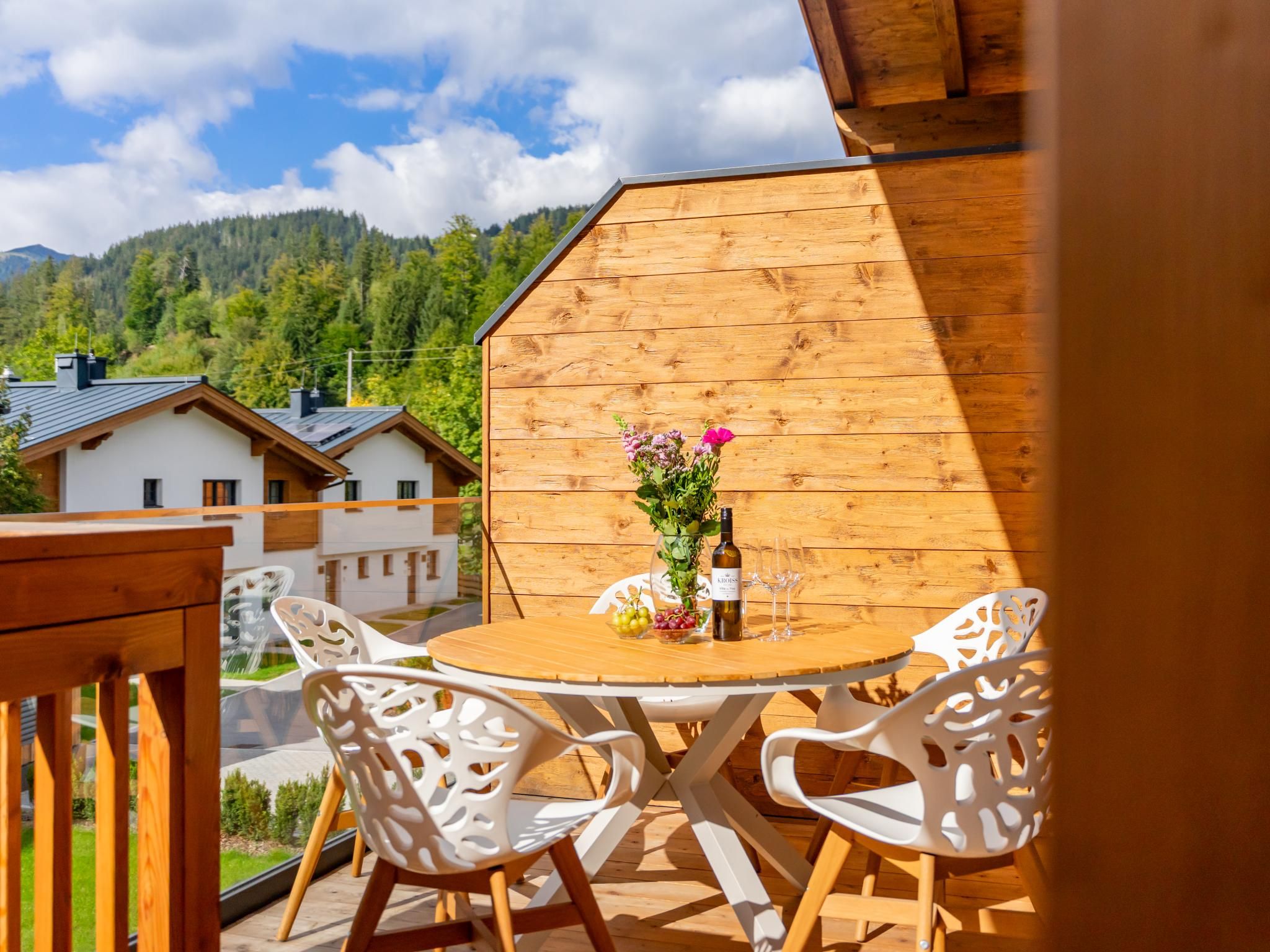 Une terrasse en bois avec une table ronde et des chaises blanches, offrant une vue sur un paysage montagneux.