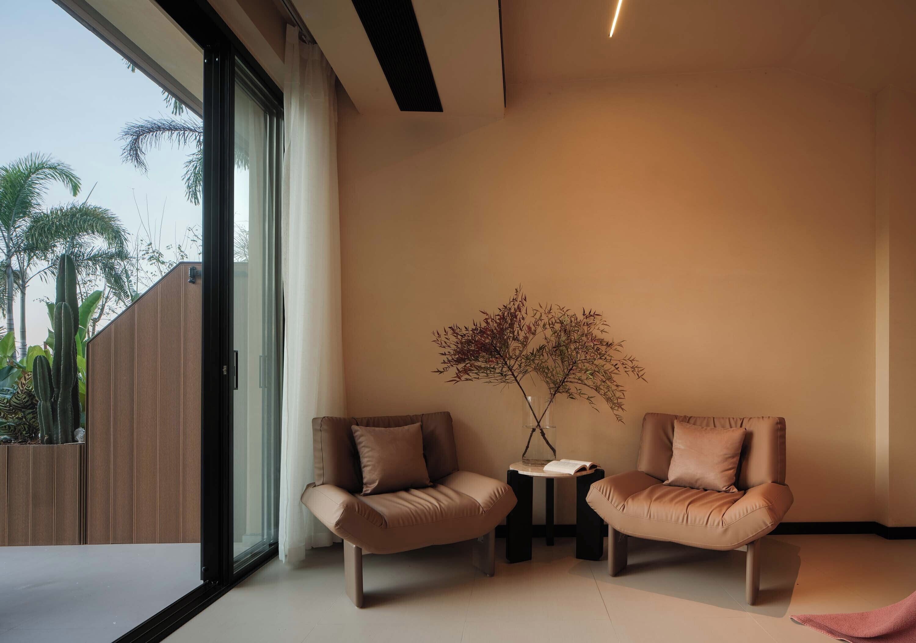 A modern room with two leather armchairs, a small table, and a vase with dried branches.