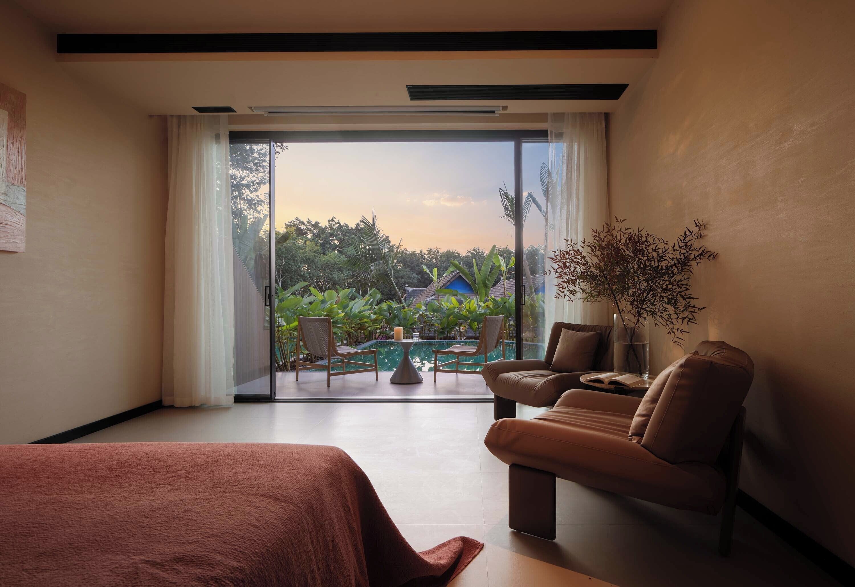 A hotel room with a large sliding glass door leading to a balcony with a pool and chairs.
