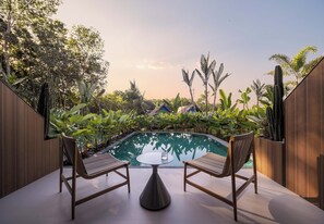 A poolside area with two wooden chairs and a table, surrounded by lush greenery and a wooden fence. - Three-Colored Cloud River Resort VILLA (Xishuangbanna Dai)
