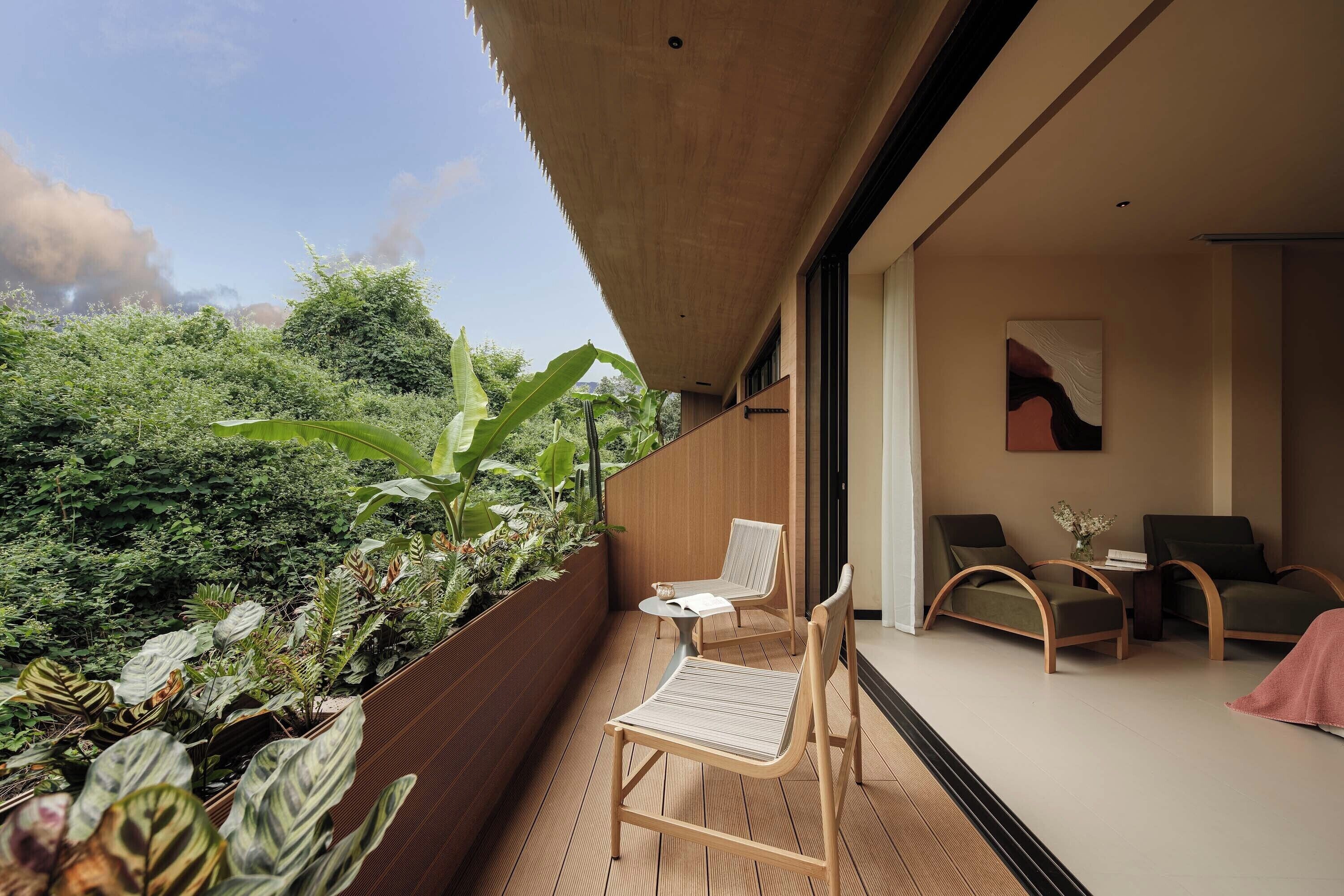 Ein Balkon mit Holzboden, zwei Stühle, einem kleinen Tisch und Blick auf üppiges Grün.
