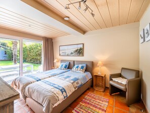 Een slaapkamer met een groot bed, een stoel, een tafeltje en een raam met uitzicht op een tuin.