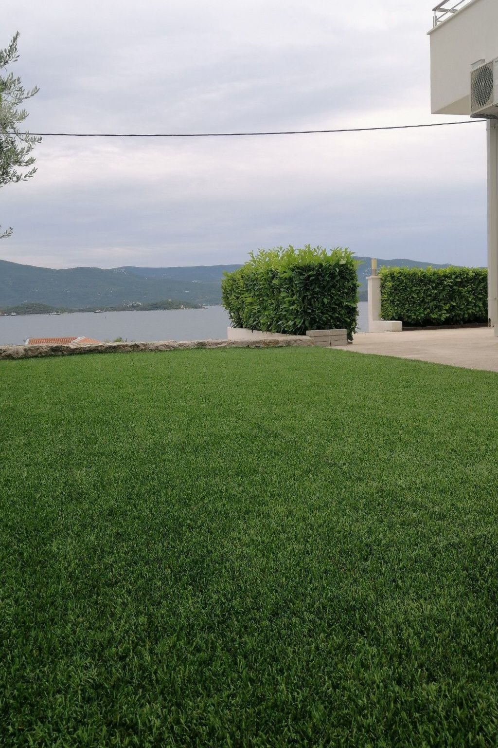 Un césped cuidado con setos y vistas a un lago y colinas al fondo.