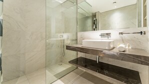 Un bagno moderno con cabina doccia in vetro, lavandino bianco e piano di lavoro in marmo.