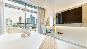 Camera d'albergo con un letto grande, una scrivania, una sedia, una televisione e vista sullo skyline della città.