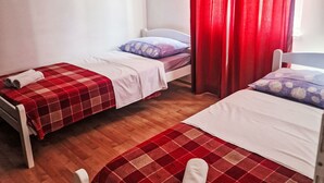 Een kamer met twee eenpersoonsbedden, elk met een rood-wit geruit sprei, witte kussens en een wit hoofdeinde.