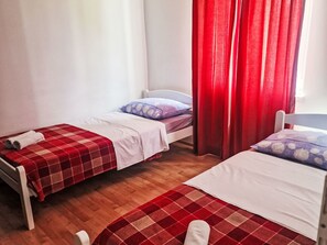 Ein Zimmer mit zwei Einzelbetten, jeweils mit einer rot-weiß karierten Bettdecke, weißen Kissen und einem weißen Kopfteil.