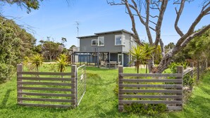 A two-story house with a fenced yard, a patio, and a large tree. - The Beach House on Sixth (Anglesea)