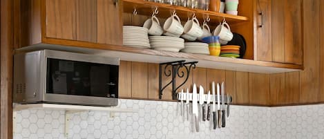 Cocina con armarios de madera, microondas, tostadora, un colgador para cuchillos y dos taburetes.