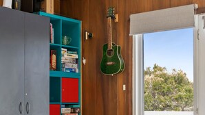 A living room with a leather sofa, a bookshelf, and a guitar. - The Beach House on Sixth (Anglesea)