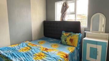 A bedroom with a bed, a nightstand, a mirror, and a window.