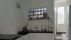 A kitchen with white cabinets, a marble countertop, a water dispenser, and a window with a grid pattern. - Rees Cabin & Homestay (Dieng Kulon)