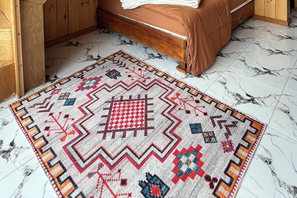 A wooden room with a bed, a patterned rug, a hanging light fixture, and a wooden staircase.