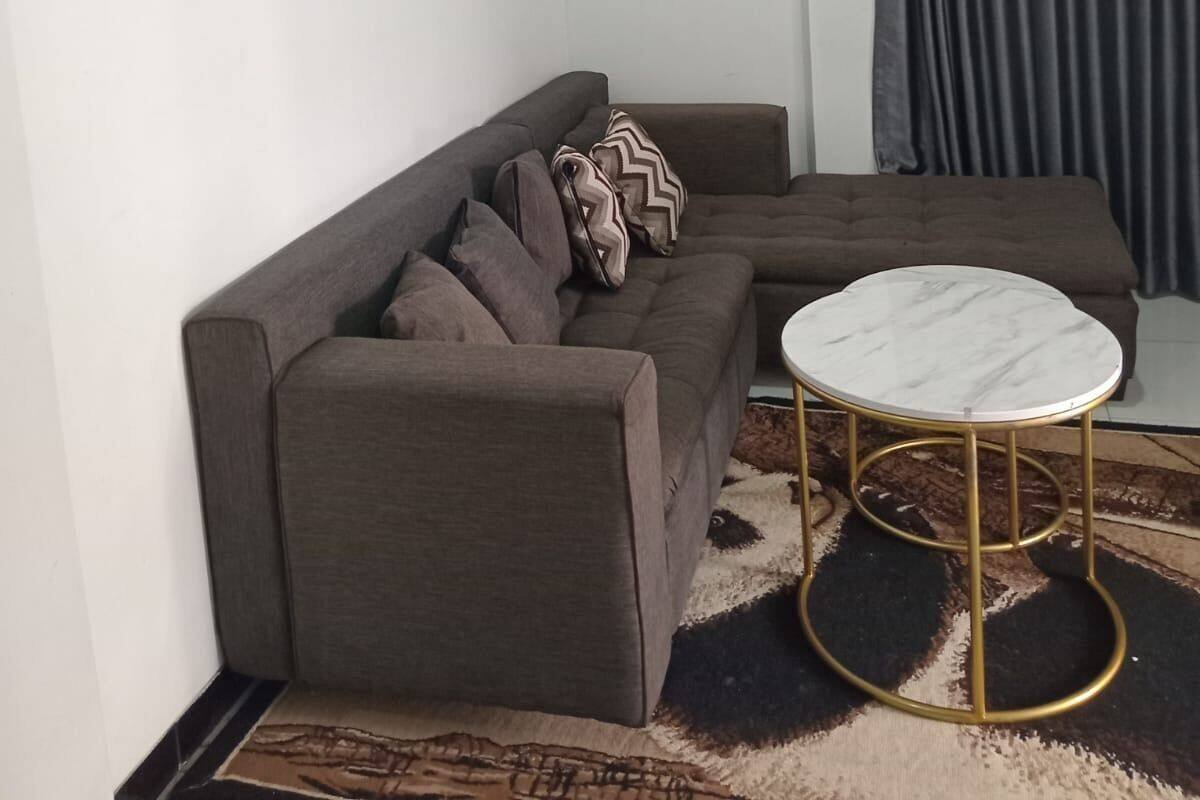 A living room with a sofa, a round coffee table, a clock on the wall, and a window with curtains.