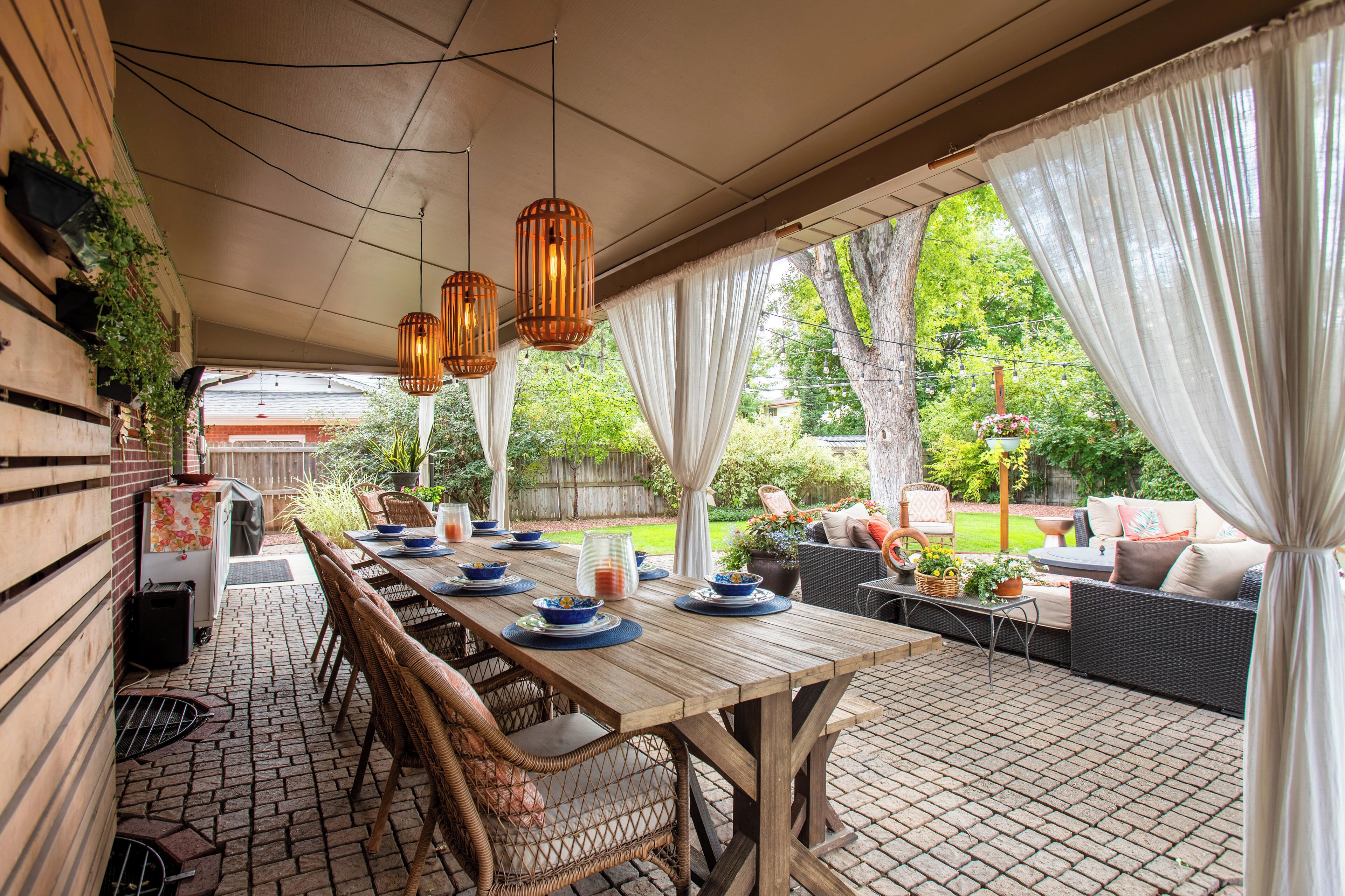 Un patio al aire libre con una mesa de madera dispuesta para comer, sillas de mimbre y un sofá de mimbre.