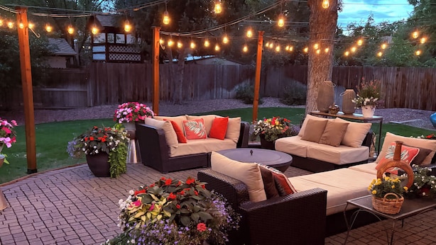 Eine Terrasse im Freien mit Korbmöbeln, Blumentöpfen und Lichterketten.