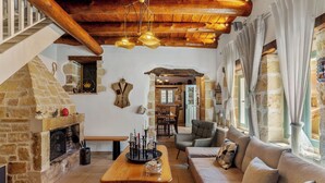 A cozy living room with a stone fireplace, wooden beams, and a sofa with cushions. - Villa Cava – Villa with a private pool in Crete (Xirostérnion)