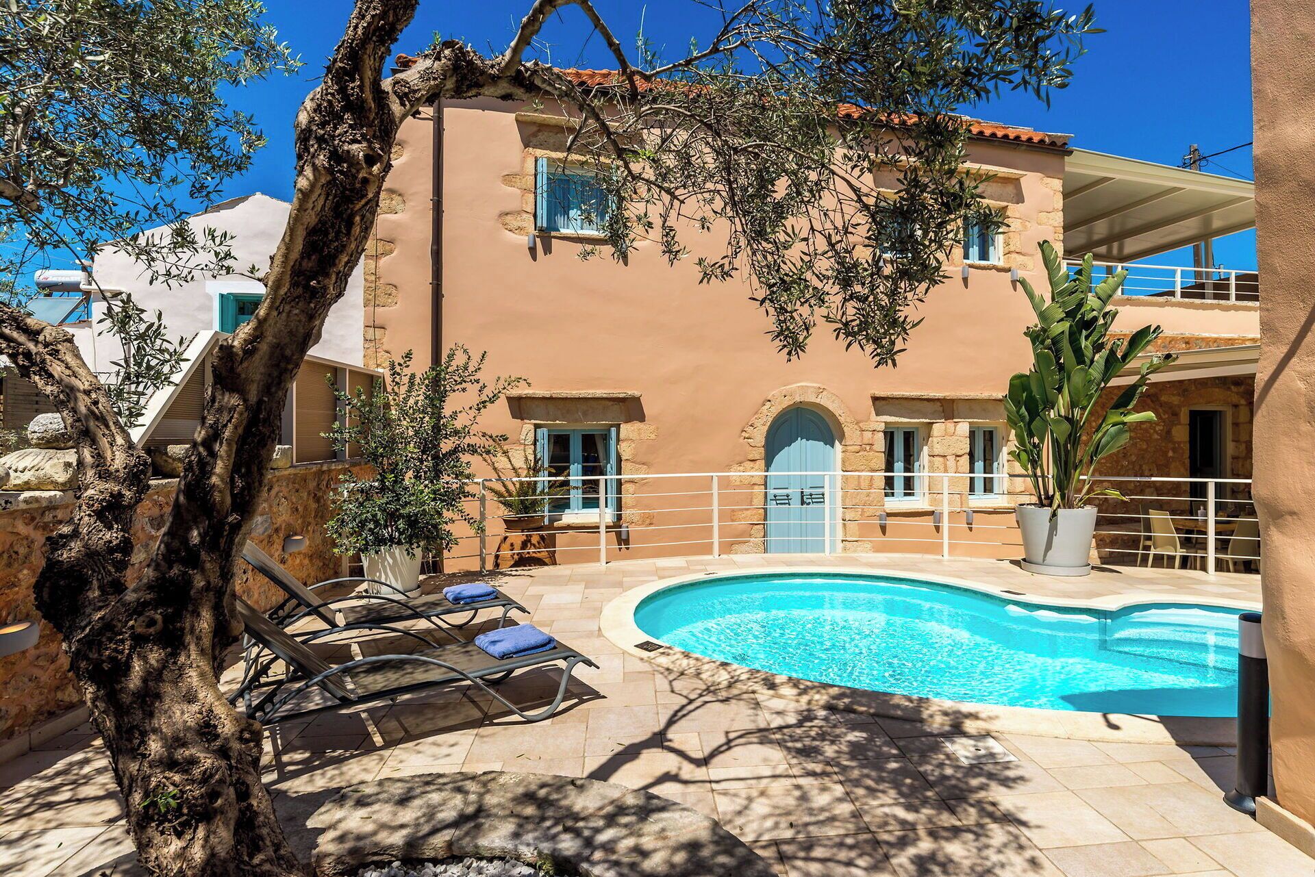 A poolside area with lounge chairs, a swimming pool, and a building with a stone facade and blue shutters.